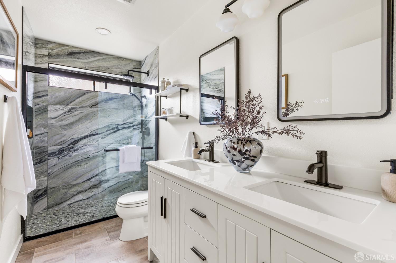 Bathroom with a double-sink vanity and a glass shower finished in dramatic gray veined stone.