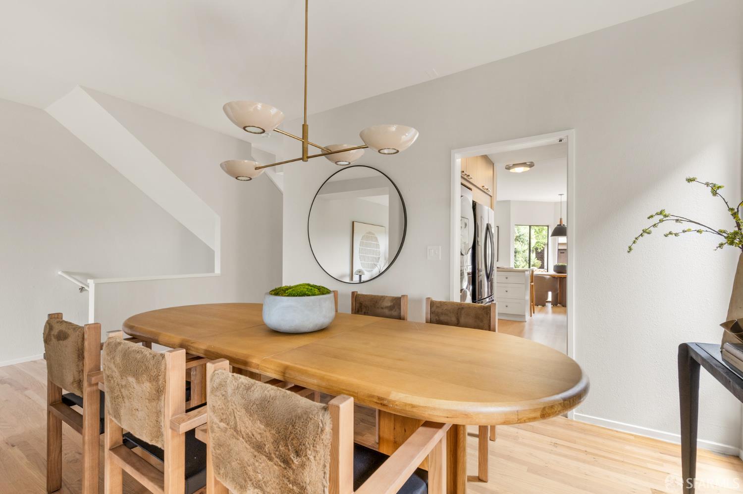 Dining room with an oval wood table, upholstered chairs, and a brass chandelier beside the kitchen doorway.