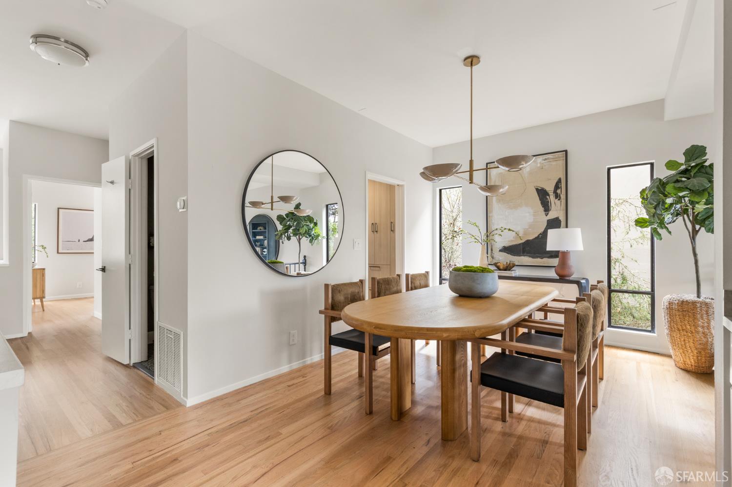 Dining room with an oval wood table, upholstered chairs, and tall windows.