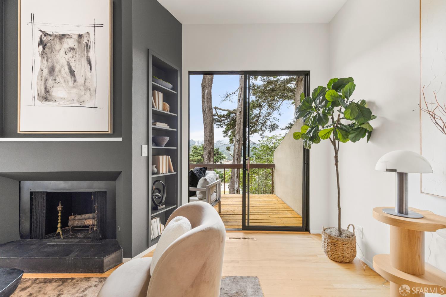 Living room with a dark fireplace and built-in shelves, opening to a tree-lined deck.