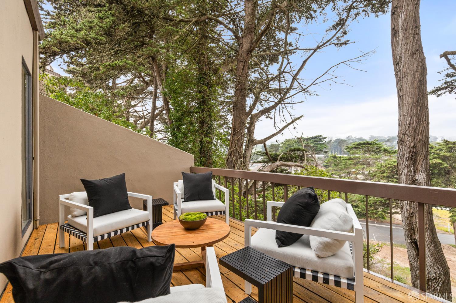 Furnished wooden deck with lounge seating beneath mature trees.