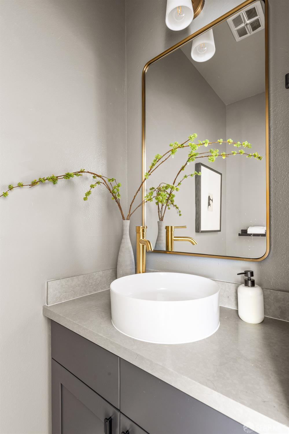 Bathroom vanity with a white vessel sink, gold faucet, and brass-framed mirror.