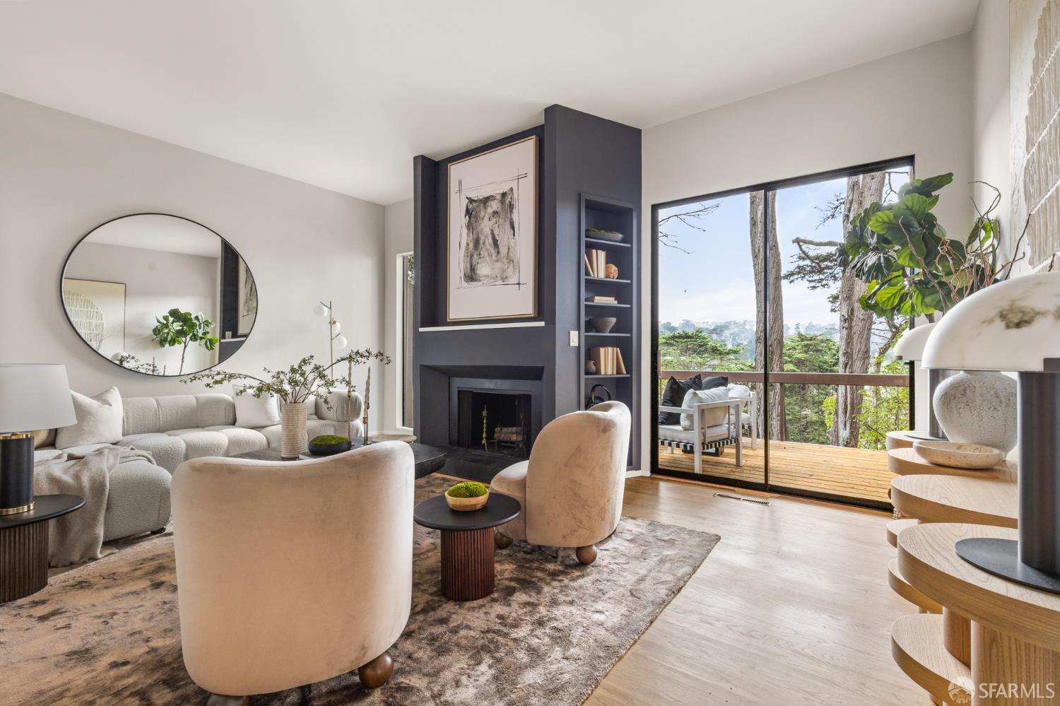 Living room with a dark fireplace wall and sliding doors opening onto a tree-lined deck.