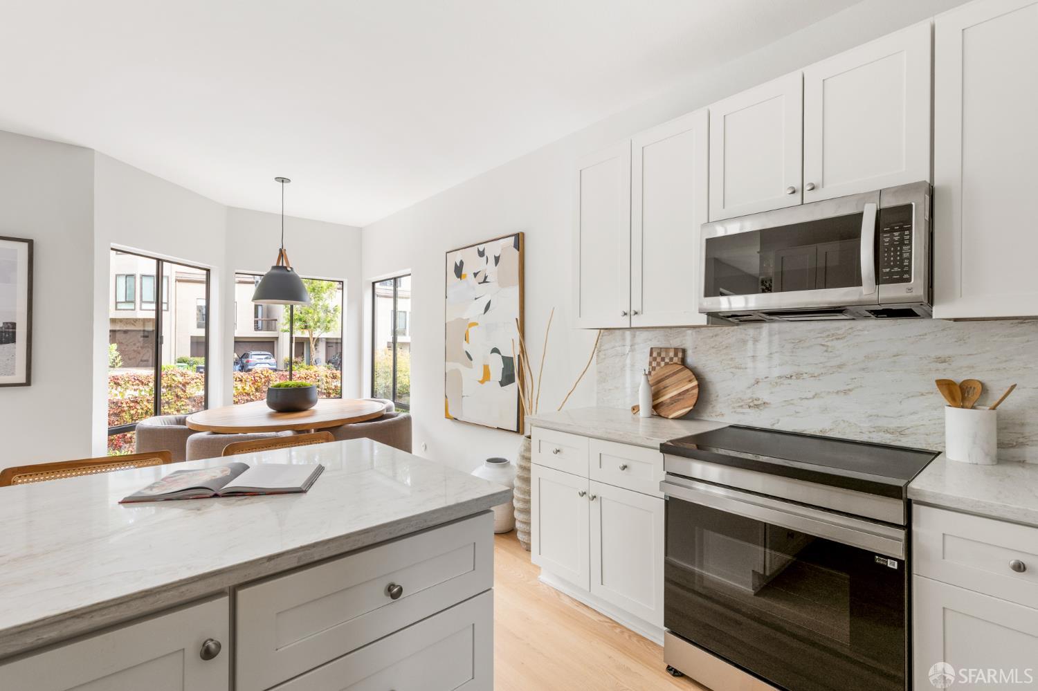 Bright white kitchen with a marble island, stainless steel appliances, and an adjoining dining area.