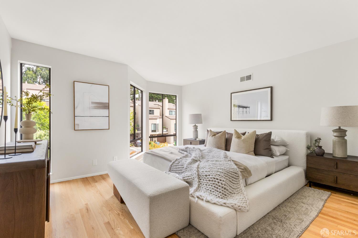 Bright bedroom with a white upholstered bed, chunky knit throw, and tall windows.