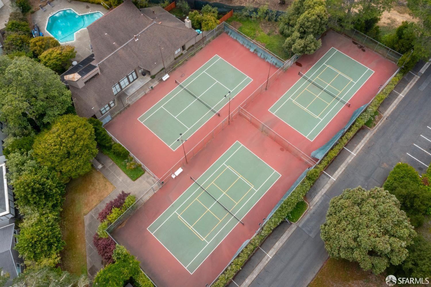 Aerial view of three tennis courts beside a swimming pool and residential buildings.