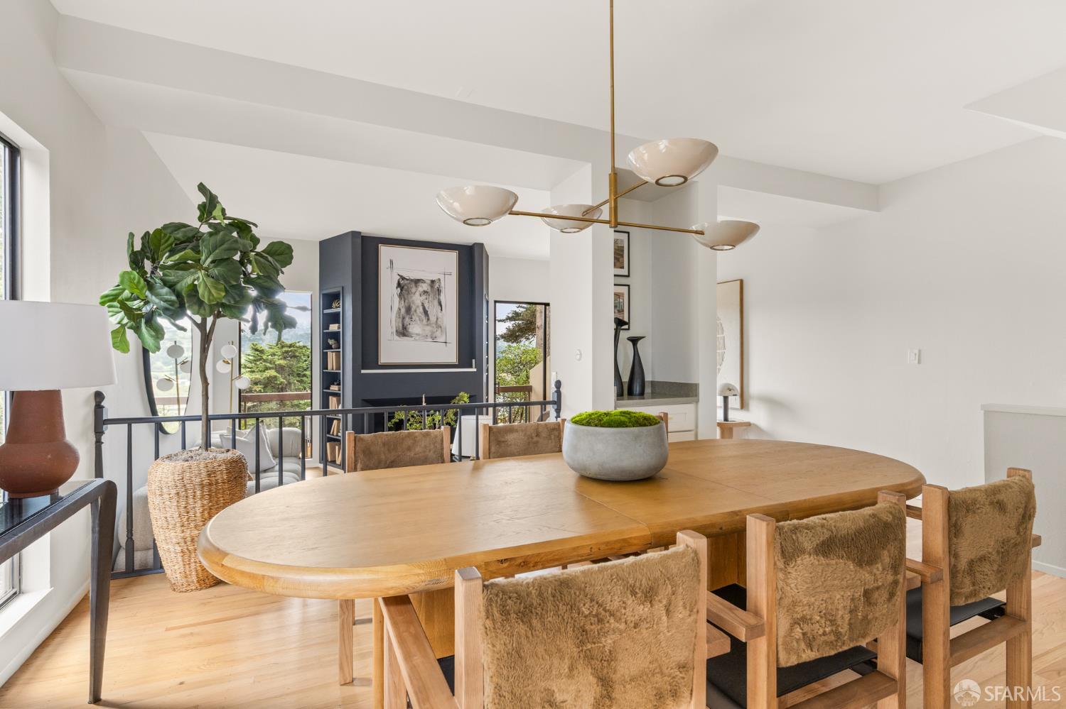 Dining room with an oval wood table, upholstered chairs, brass chandelier, and dark built-in shelving.