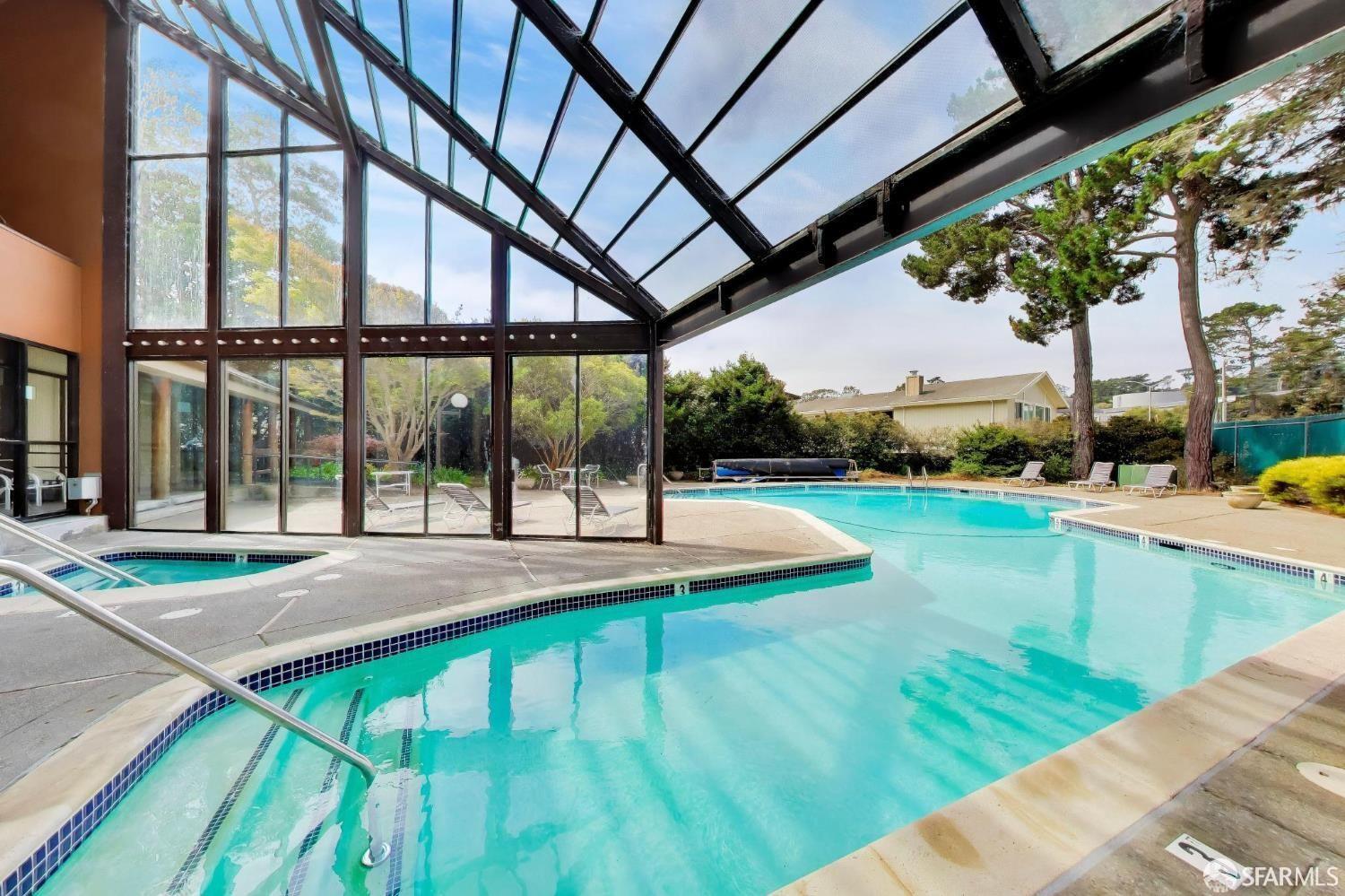 Swimming pool and spa beneath a glass-and-steel enclosure, opening onto a sunny outdoor deck.