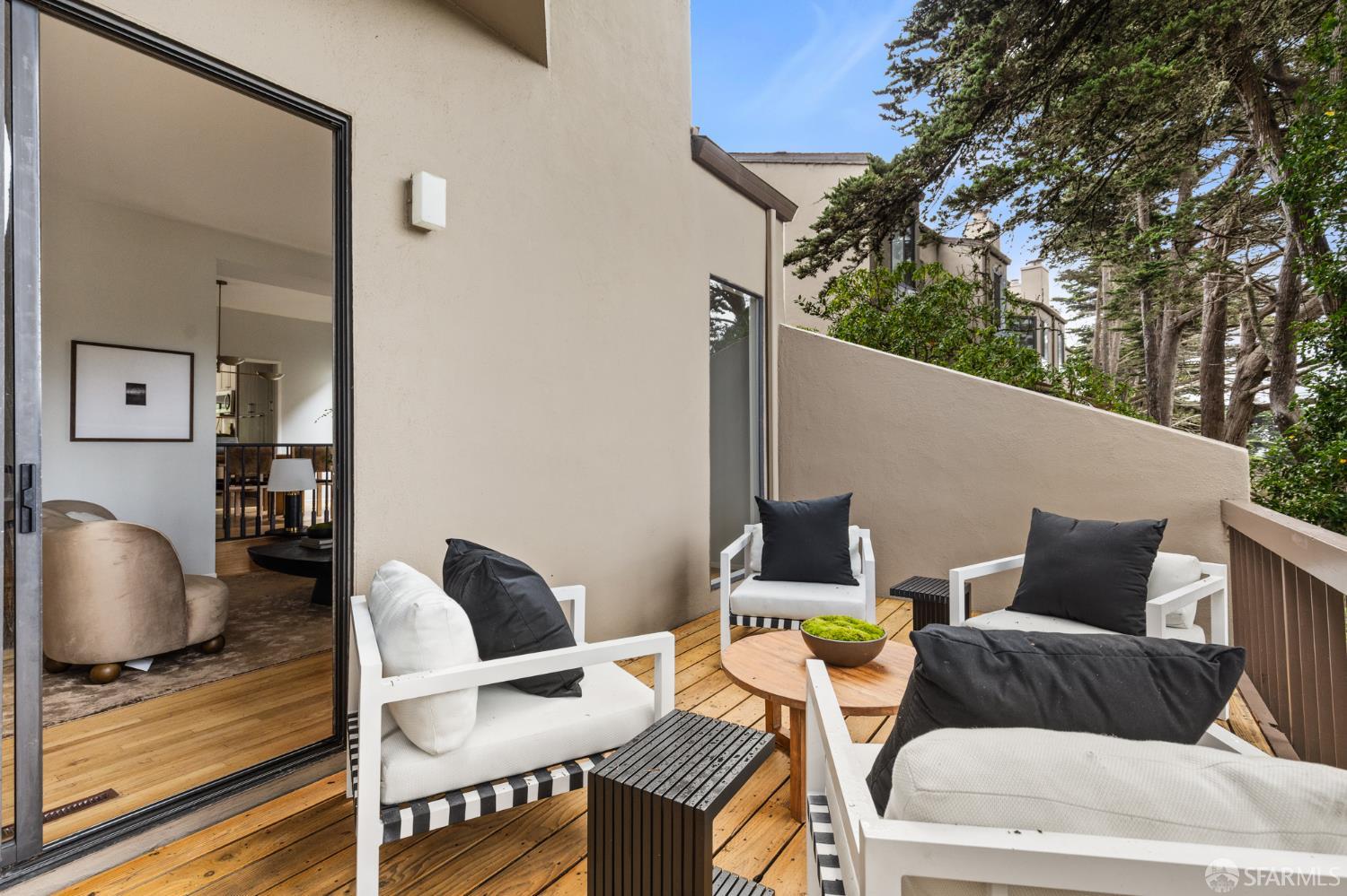 Furnished wood deck with white lounge chairs and a round coffee table, framed by evergreen trees.