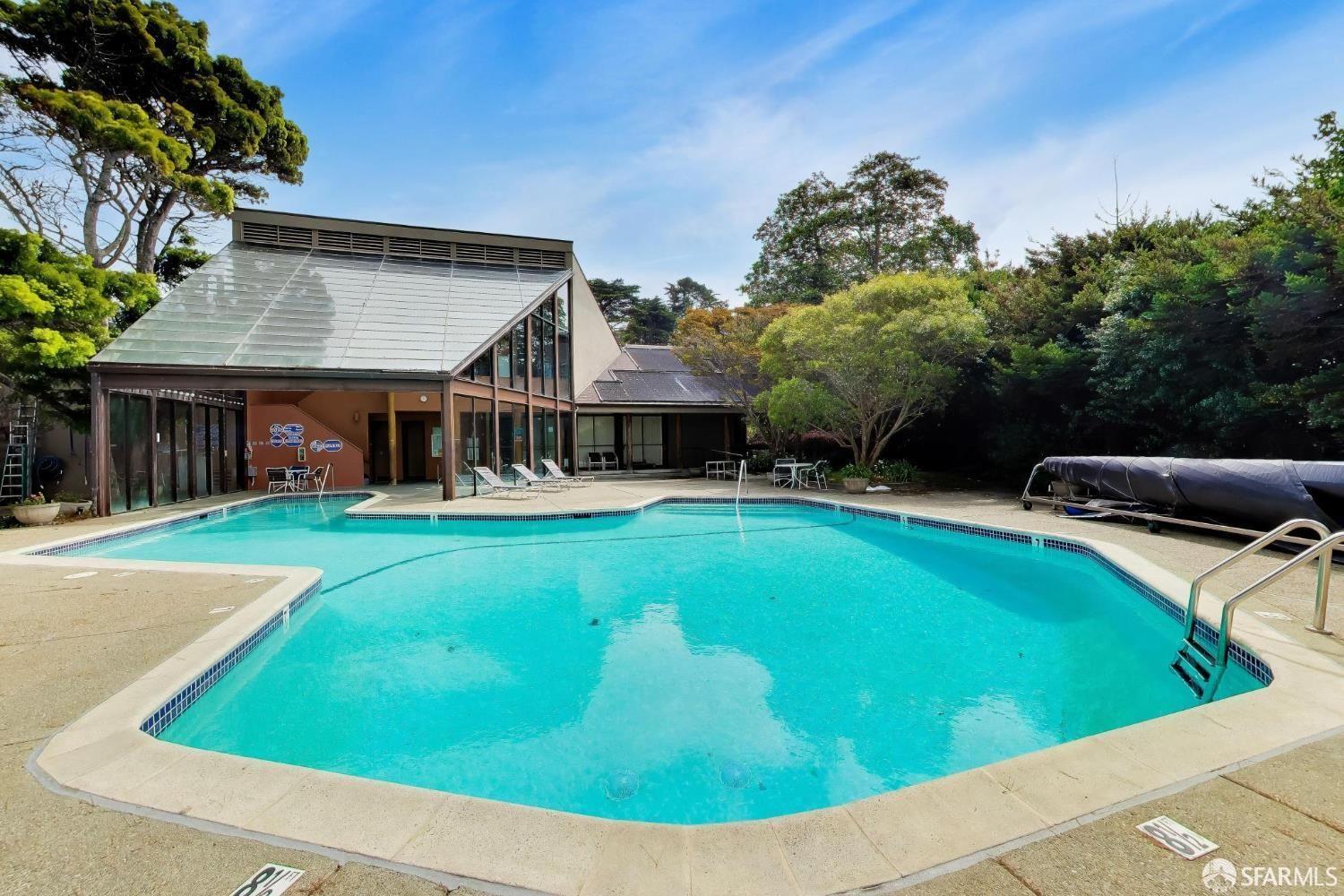 Outdoor swimming pool beside a glass-walled pavilion, with lounge chairs and a concrete deck.