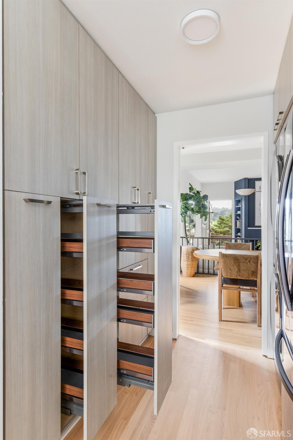 Kitchen pantry with open pull-out drawers and a dining area visible through the doorway.