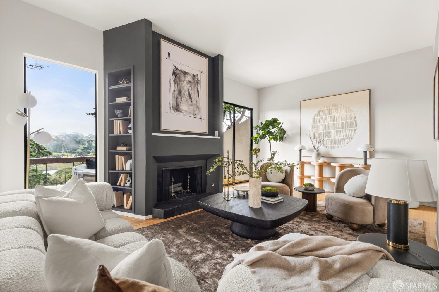 Living room with a charcoal fireplace, built-in shelves, neutral seating, and windows overlooking greenery.