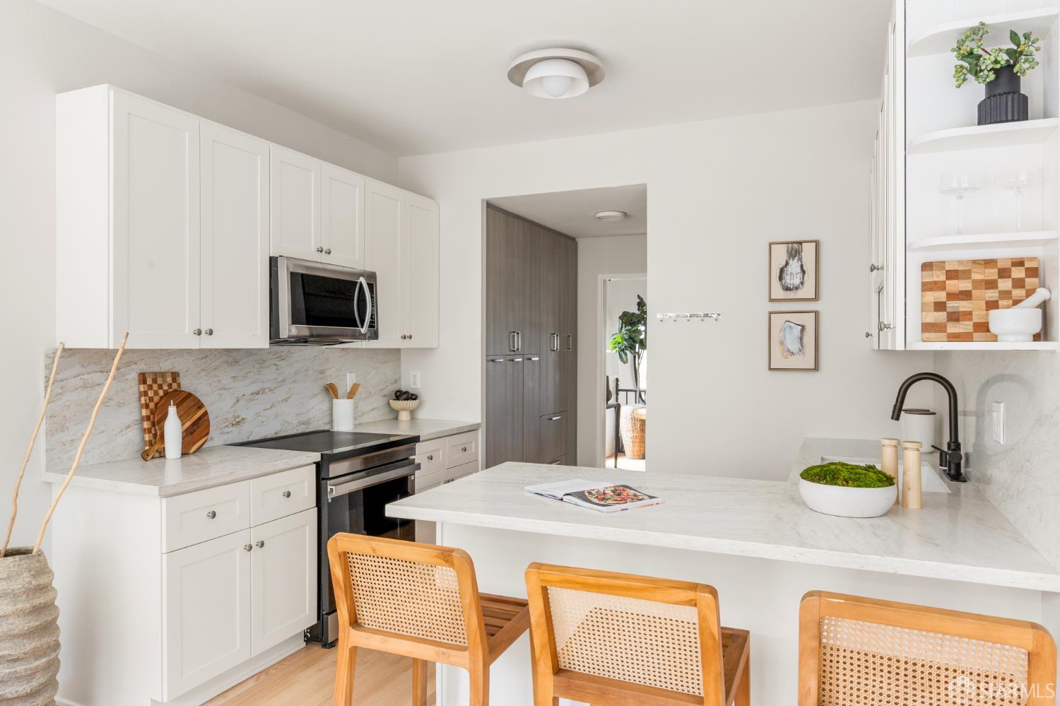Bright kitchen with white cabinetry, marble-look counters, stainless appliances, and a large island with cane-back chairs.
