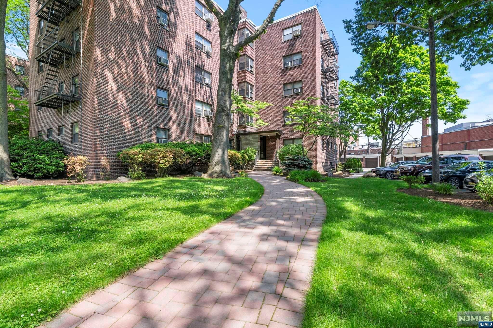 Brick apartment building behind a curved walkway, landscaped lawn, and mature trees.