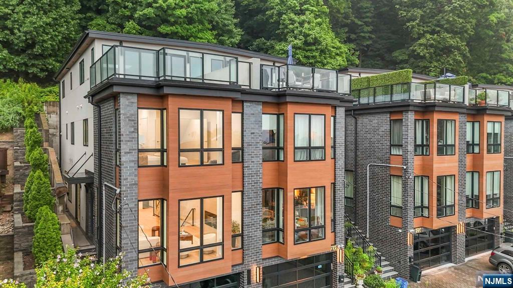 Modern attached homes with glass rooftop terraces and orange-toned façades, backed by trees.
