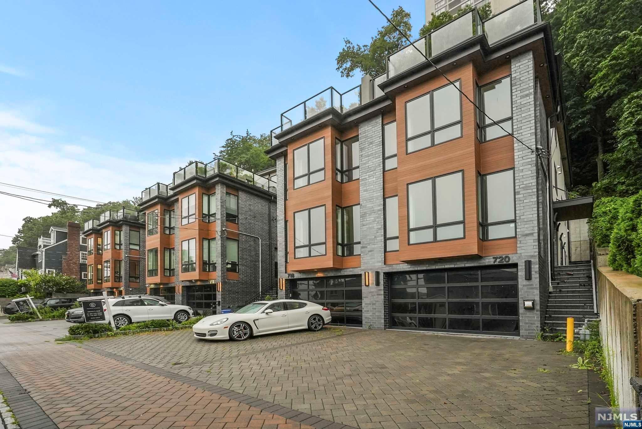 Modern multi-story residence with wood-look cladding, rooftop terraces, and a paved driveway.