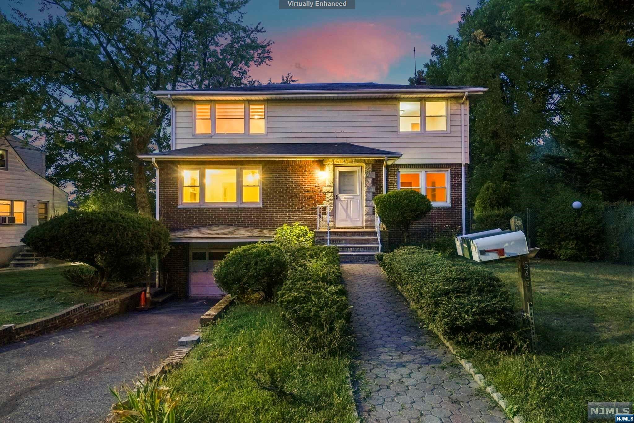 Two-story brick-and-siding house at dusk, with glowing windows and a stone walkway through the front garden.