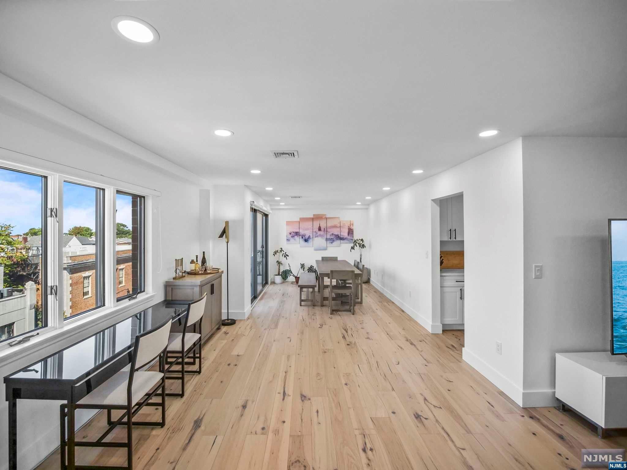 Open-plan dining and living area with pale wood floors, large windows, and a furnished dining table.