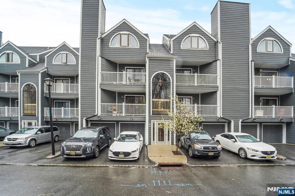 Gray condominium building with balconies and arched windows, viewed from the street with cars parked in front.