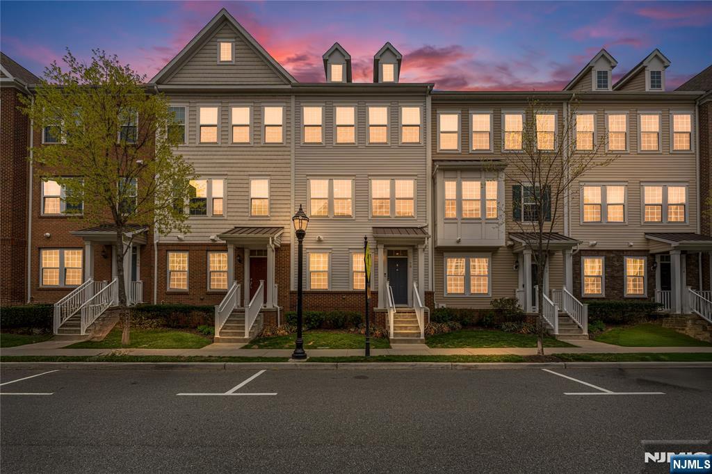 Attached townhomes with illuminated windows and entrance steps beneath a pink dusk sky.