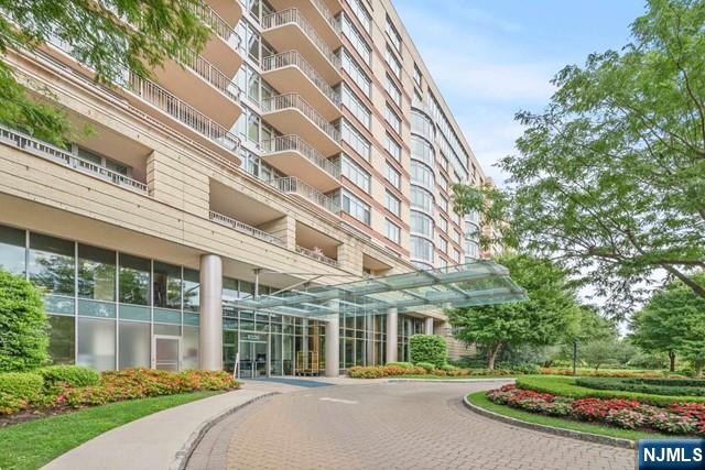 Condominium entrance with a glass canopy, curved driveway, and landscaped grounds.