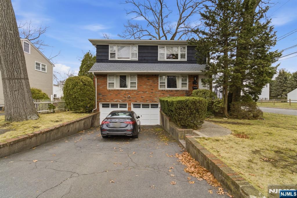 House with a brick facade, dark upper siding, attached garage, and a car in the driveway.