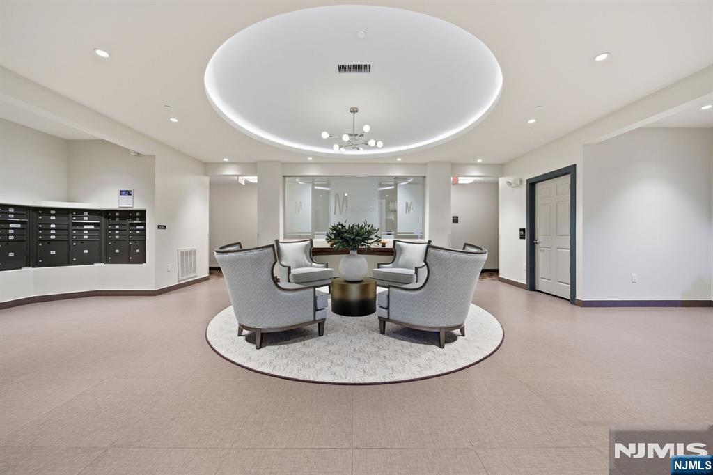 Furnished lobby with gray lounge chairs around a table, mailboxes, and a circular recessed ceiling feature.