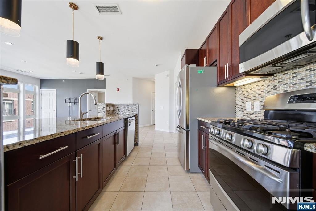 Modern kitchen with a granite island, dark wood cabinets, and stainless steel appliances.