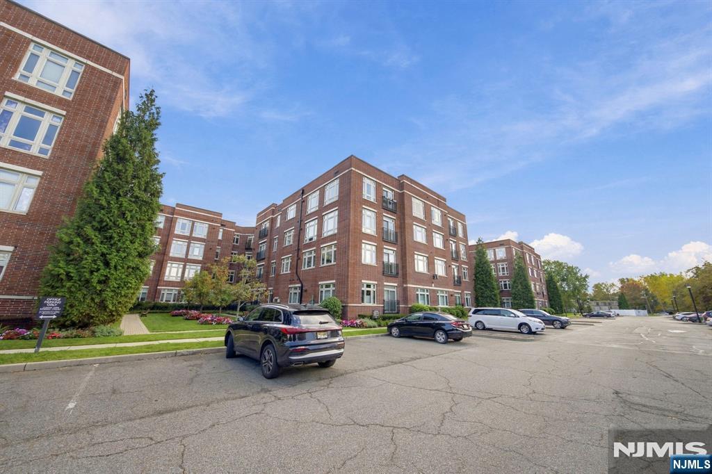 Red-brick residential building with landscaped grounds and a parking lot in front.