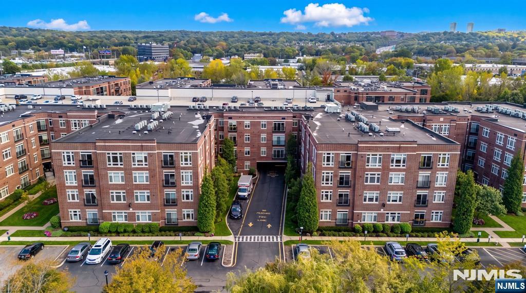 Brick apartment buildings surround a central entrance drive, with parking and wooded hills beyond.
