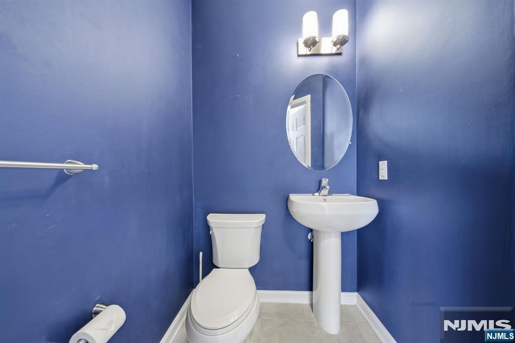 Bathroom with deep blue walls, a white toilet, and pedestal sink beneath an oval mirror.