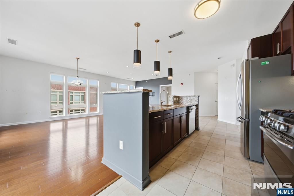 Open-plan kitchen with dark cabinetry, stainless steel appliances, and a peninsula beside a bright living area.