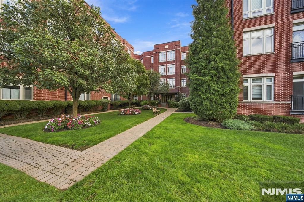 Red-brick apartment building around a landscaped courtyard with a paved walkway and flower beds.