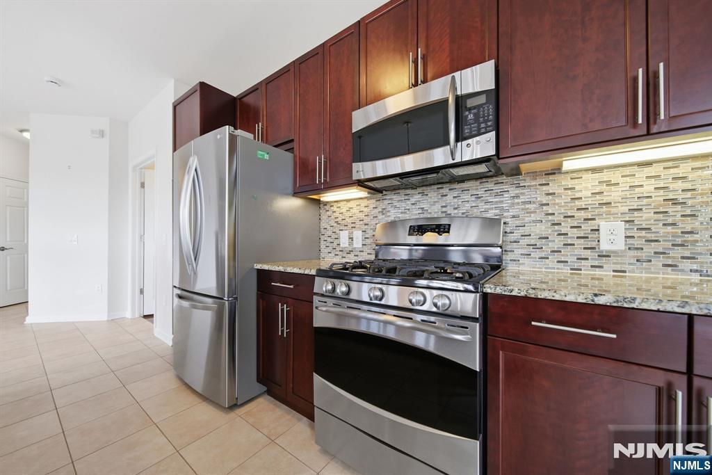 Kitchen with dark wood cabinets, stainless steel appliances, and a mosaic tile backsplash.