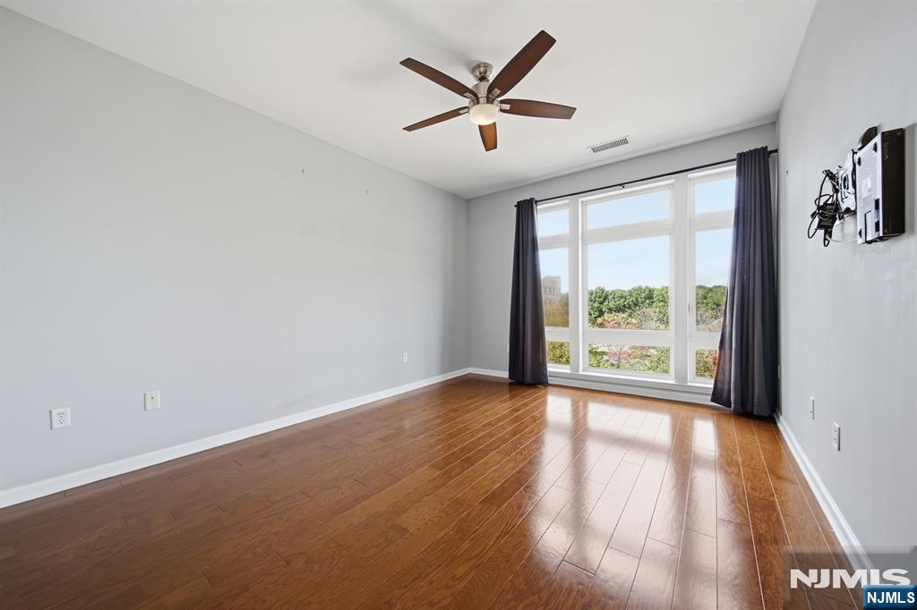 Empty room with hardwood floors, a ceiling fan, and large curtained windows.