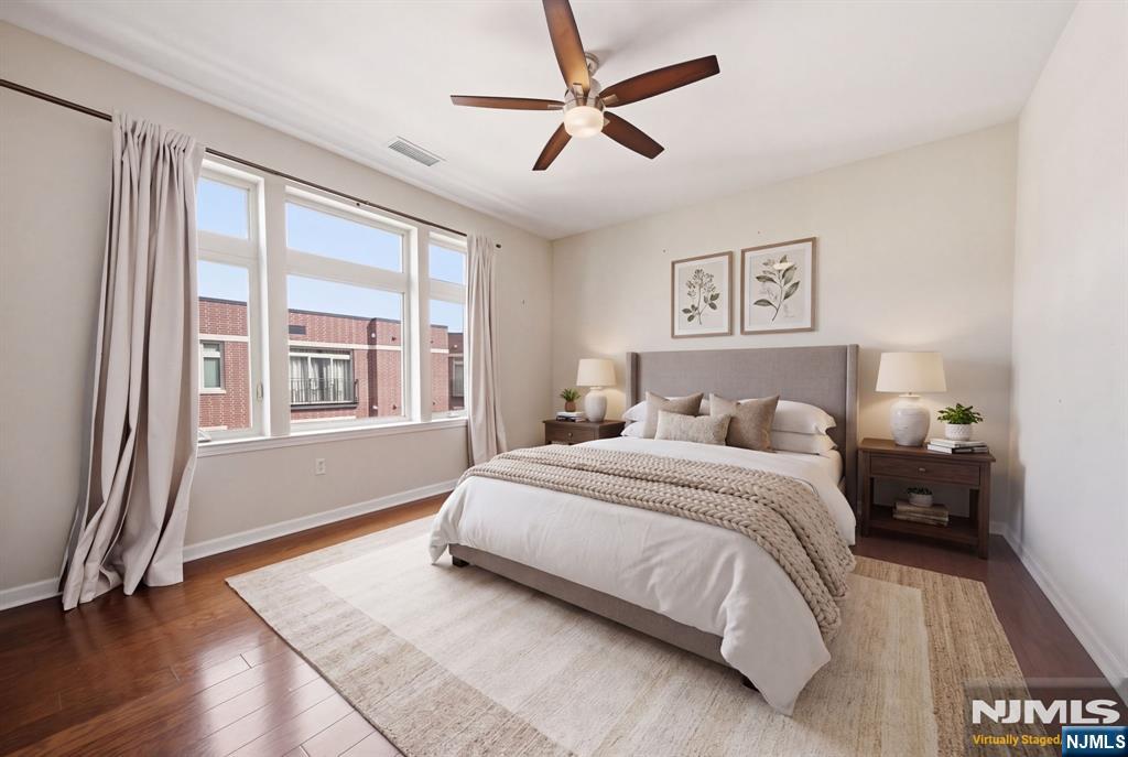 Staged bedroom with a king-size bed, large curtained windows, and hardwood floors.