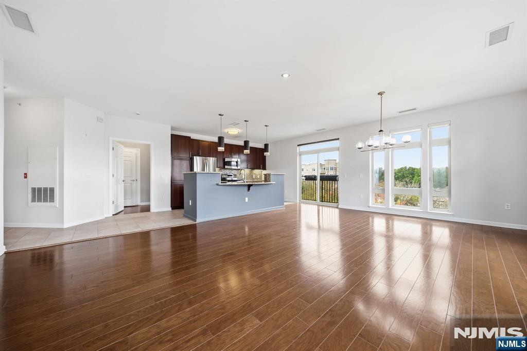 Vacant open-plan living room with hardwood floors, kitchen breakfast bar, and large windows opening to a balcony.