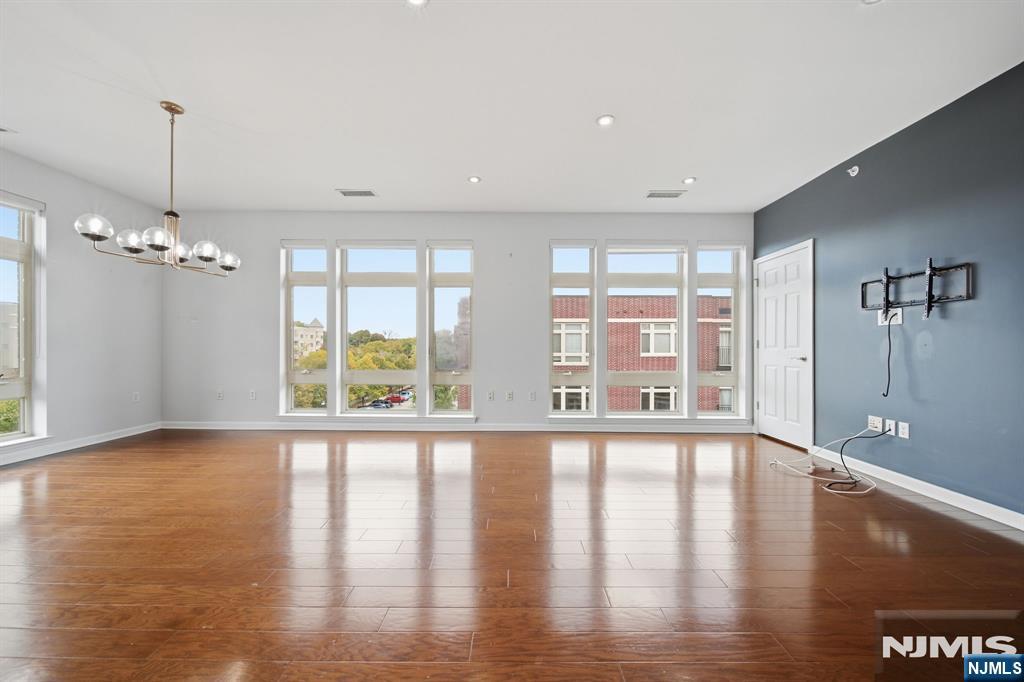 Vacant living room with hardwood floors, tall windows, chandelier, and dark blue accent wall.