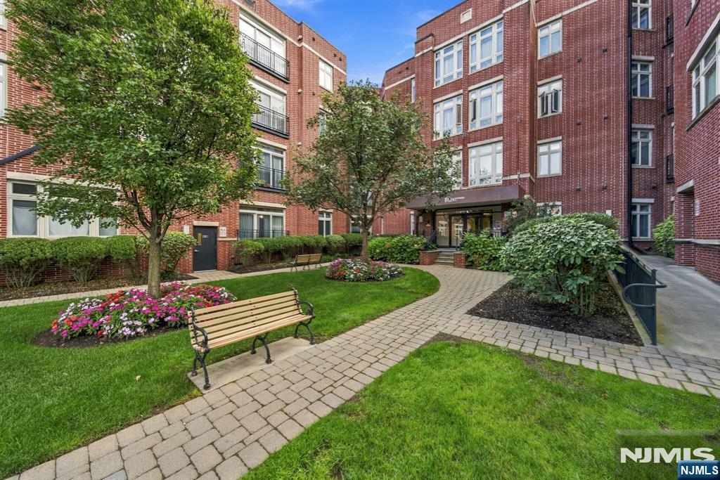 Apartment building courtyard with a paved walkway, flower beds, lawn, and benches.