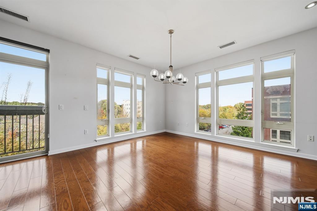Bright empty room with hardwood floors, a chandelier, tall windows, and a balcony.