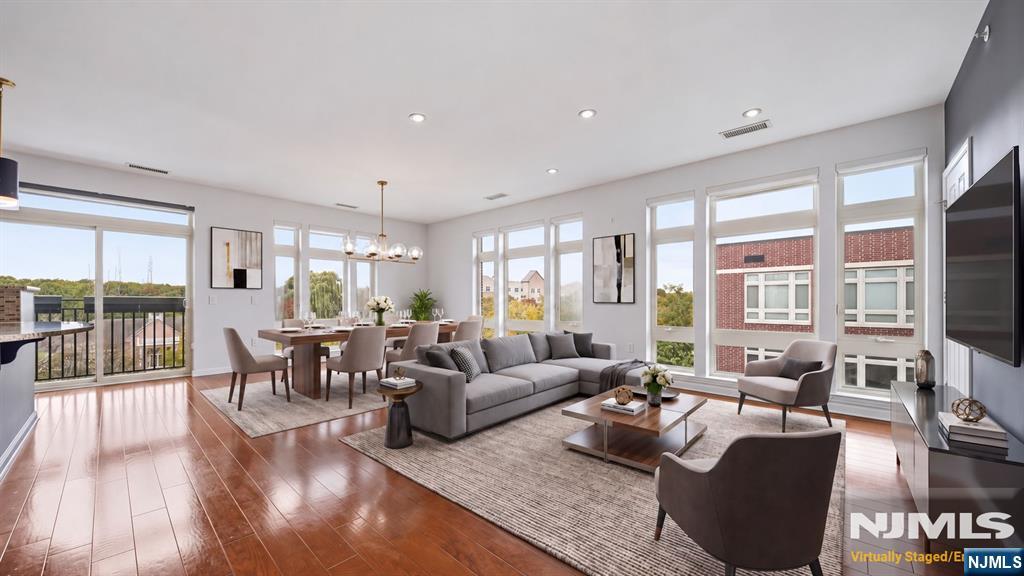 Open-plan living and dining room with a gray sectional, hardwood floors, and large windows.