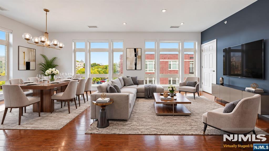 Open-plan living and dining room with large windows, hardwood floors, and staged seating.