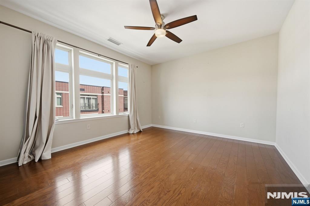 Empty room with hardwood floors, a ceiling fan, and large curtained windows.