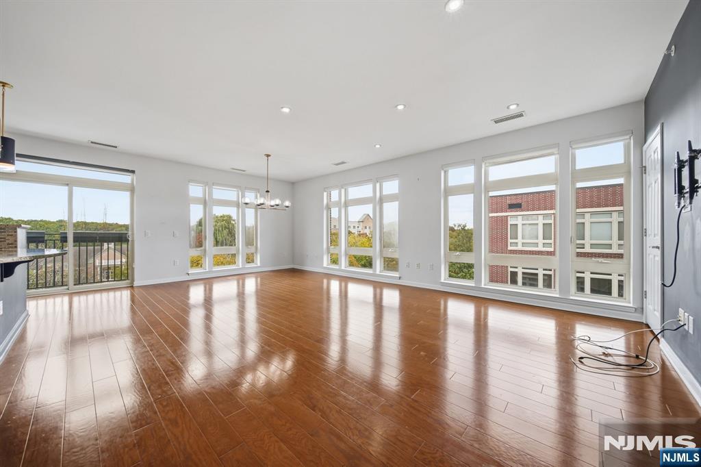 Vacant living room with glossy hardwood floors, tall windows, and a sliding glass door to the balcony.