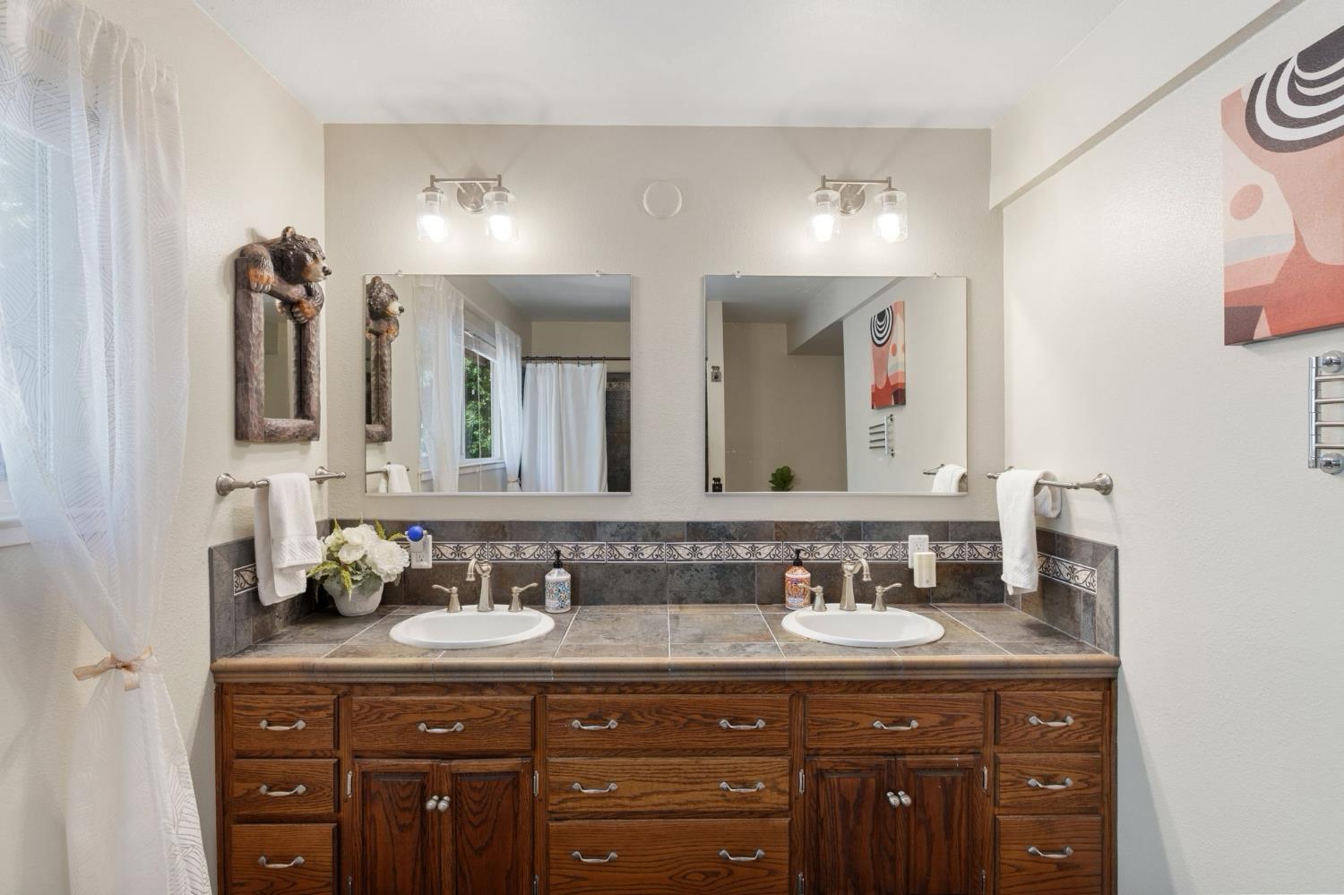 Bathroom vanity with two sinks, dark wood cabinetry, tiled counters, and large mirrors.
