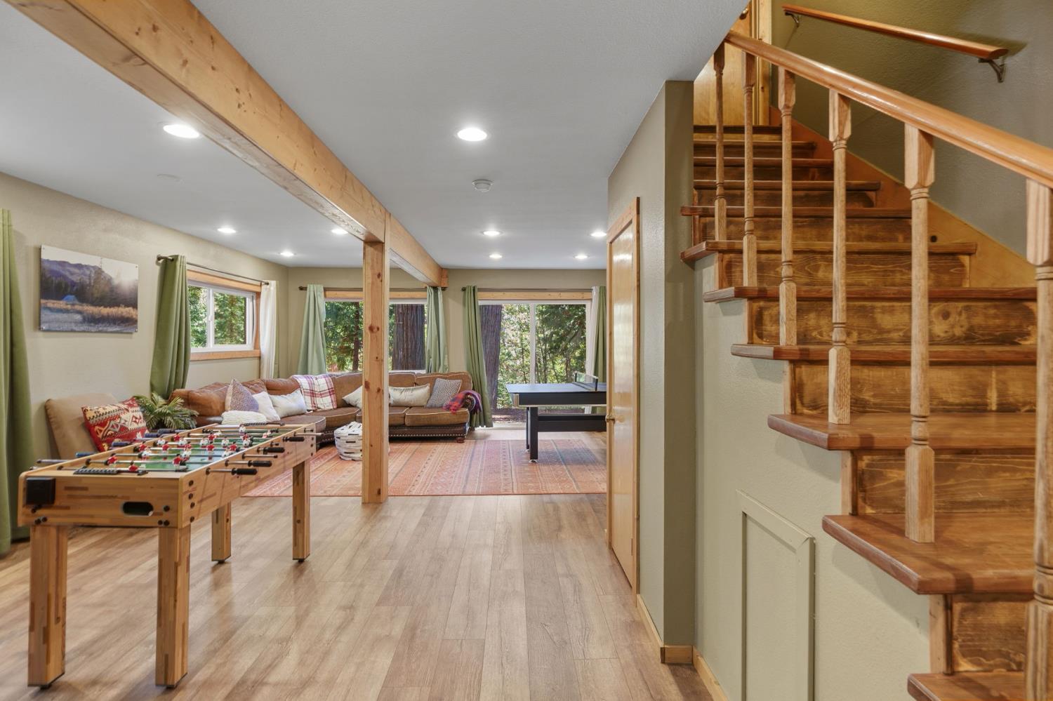 Game room with foosball and ping-pong tables, sofas, and a prominent wooden staircase.