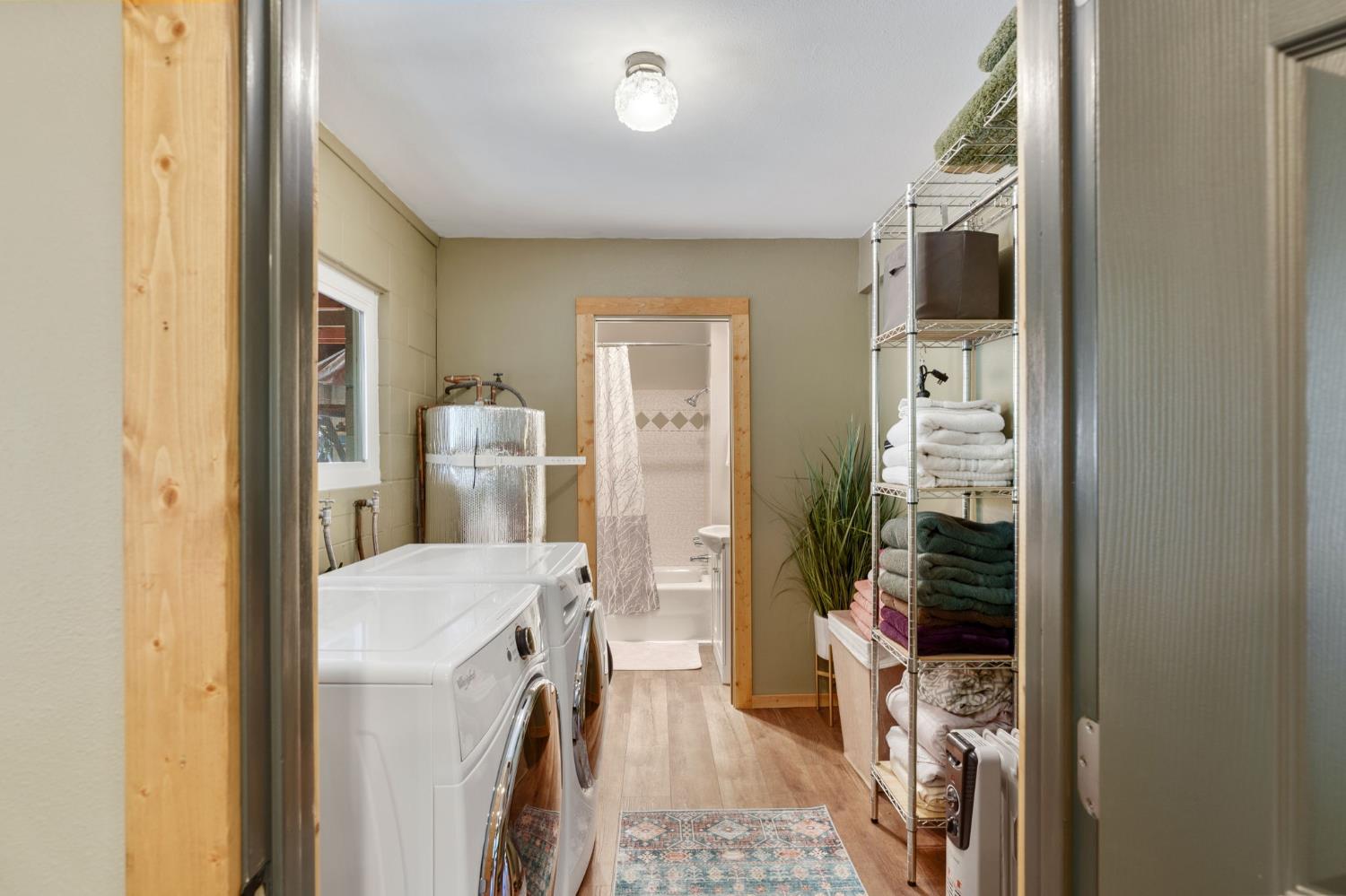 Laundry room with two white machines and towel shelves, looking through to a bathroom with a tub.