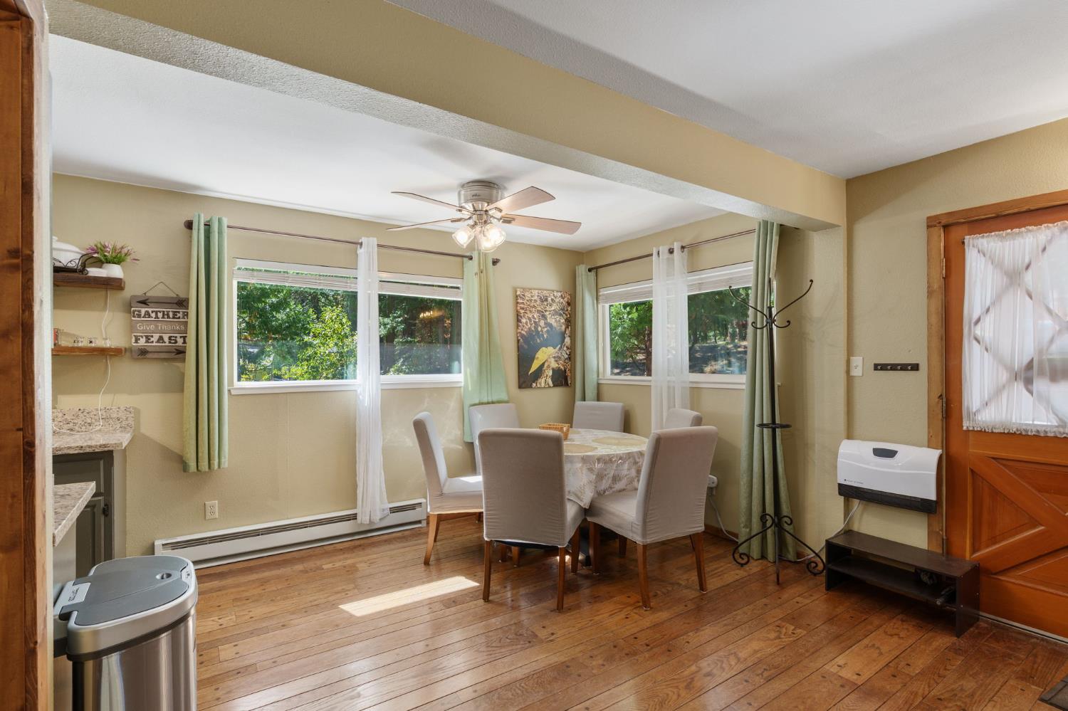 Dining area with a table, hardwood floors, and windows framed by green curtains.