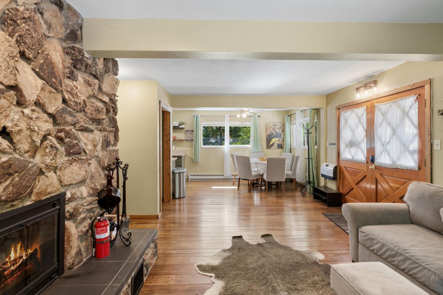 Living room with a floor-to-ceiling stone fireplace and hardwood floors, opening to a dining area.