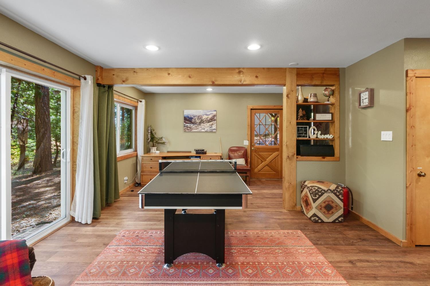 Game room with a ping-pong table, patterned rug, wood beams, and sliding glass doors.